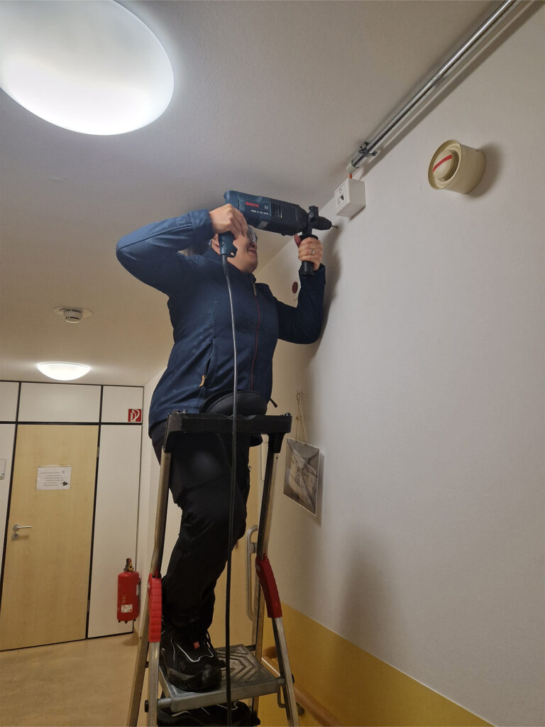 Women working with a drill on a ladder.