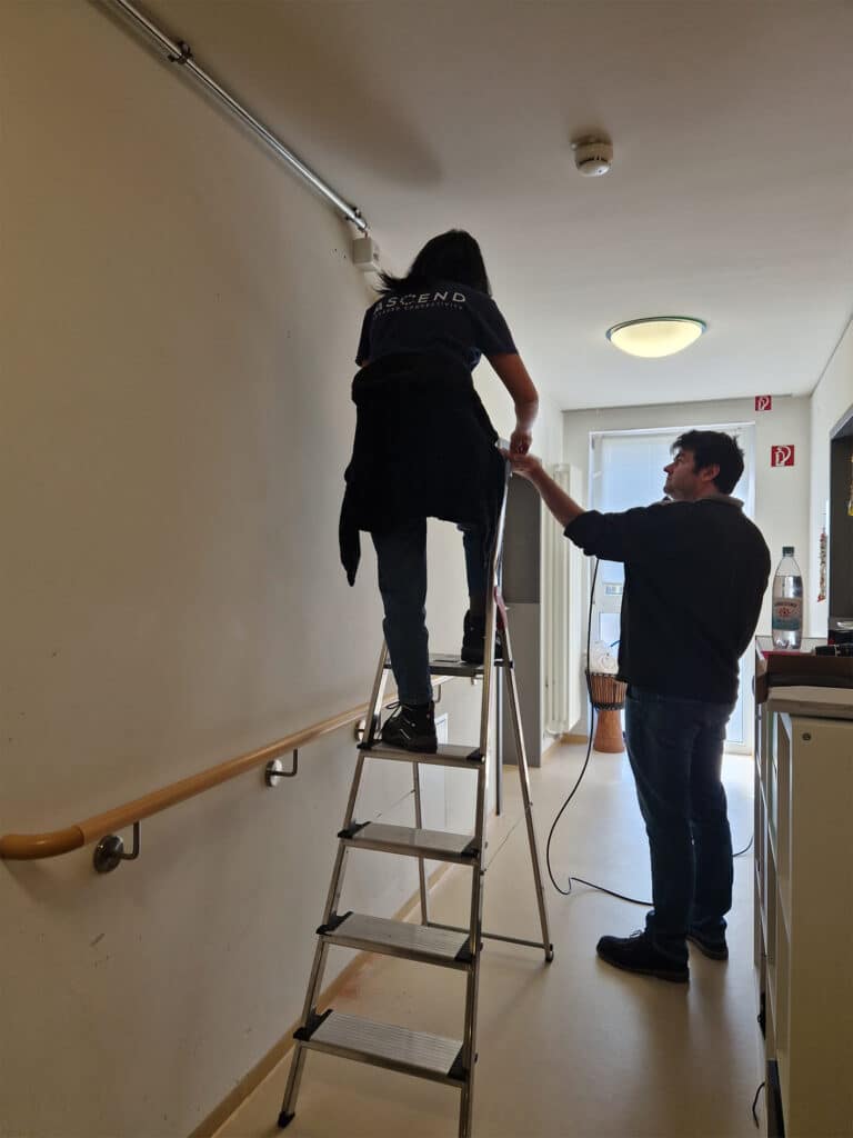 Man supports woman on ladder during installation work.